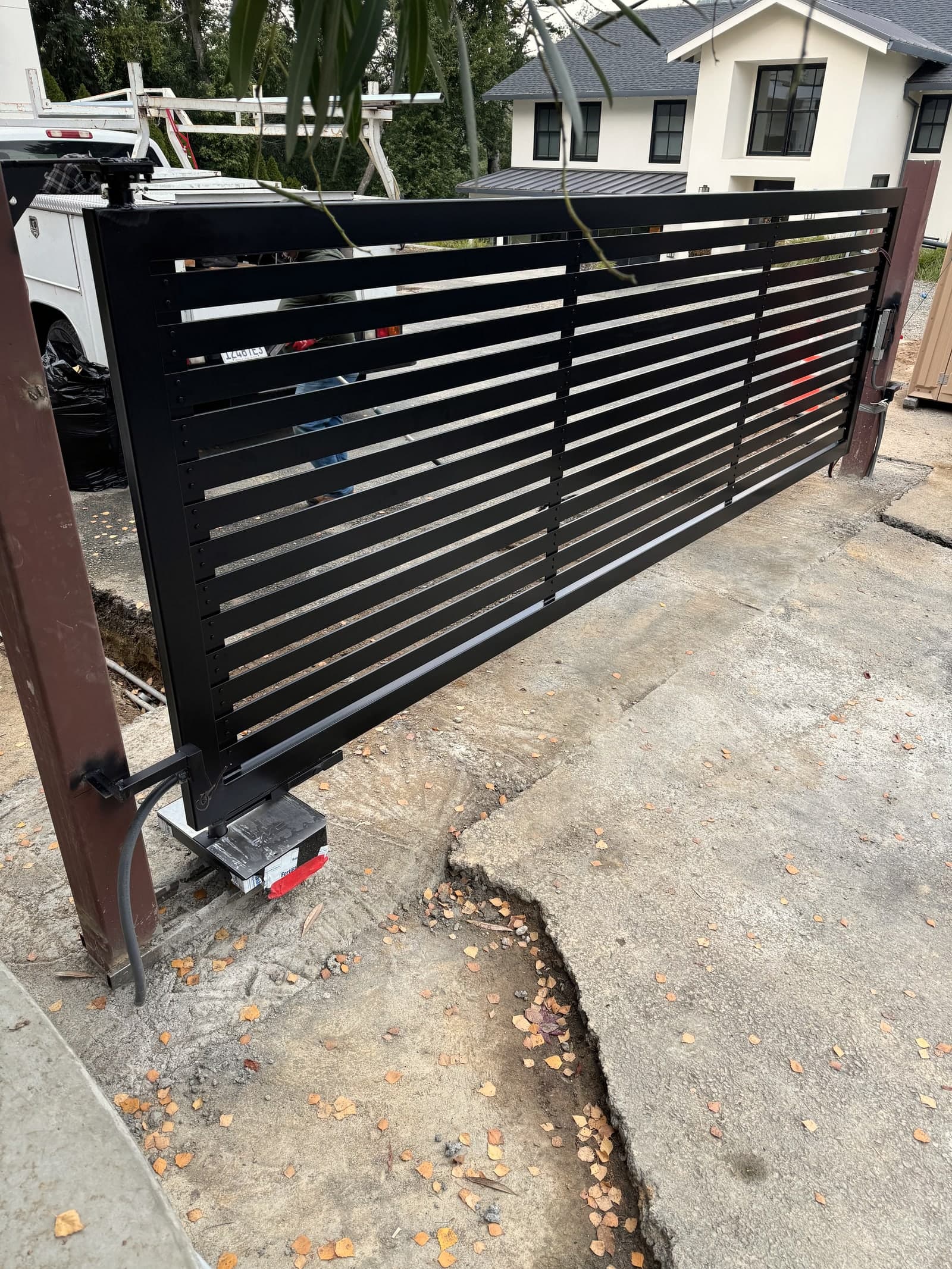 Black metal driveway gate with horizontal slats and hardware.